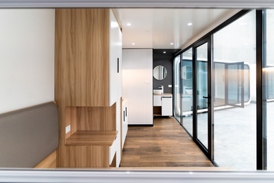 WhiteHouse Spacee design interior with bed frame, wood-look storage unit with white cupboard doors and black cupboard handles, glass doors with black door frame and modern bathroom fixtures.