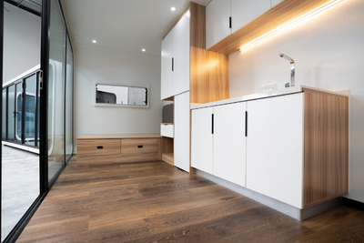 WhiteHouse Spacee design interior with laminate plank flooring, wooden bedframe, fully installed kitchenette with functioning tap and power points, white cupboard doors with black cupboard door handles.