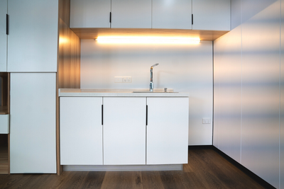 WhiteHouse Spacee design interior with laminate plank flooring and fully installed kitchenette with functioning tap and power points, white cupboard doors with black cupboard door handles and under cupboard LED lights.