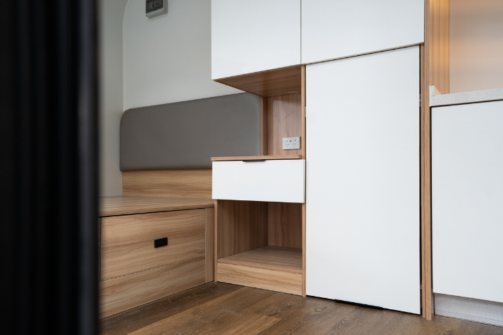 WhiteHouse Spacee design interior with laminate plank flooring and fully installed bedframe, various storage compartments with white cupboard doors with black cupboard door handles and under cupboard LED lights.