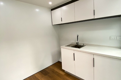 Eat Spacee design interior with fully installed kitchenette with top shelf and under table storage with white cupboard doors and black handles and laminate plank flooring.