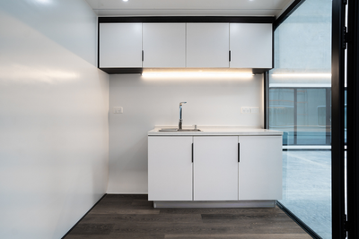 Eat Spacee design interior with fully installed kitchenette with top shelf and under table storage with white cupboard doors and black handles and laminate plank flooring and under cupboard LED light.