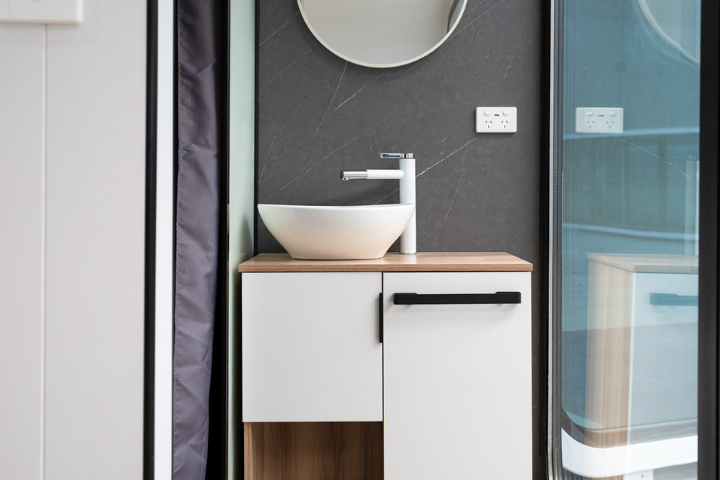 Wash Spacee design interior with fully installed modern bathroom fixtures including modern bowl sink, round mirror and white cupboard doors with black handles and white power point. 